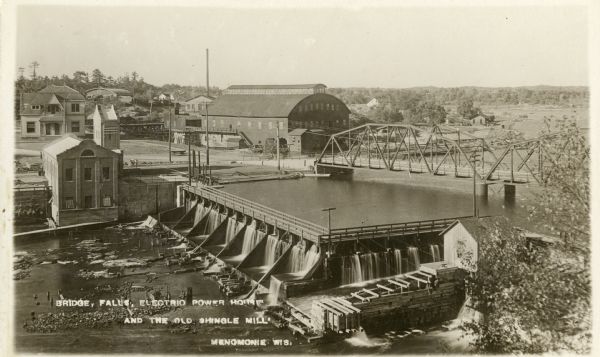 Elevated view of the dam on the Red Cedar River, also showing the electric power plant and mills. Caption reads: "Bridge, Falls, Electric Power House and the Old Shingle Mill, Menomonie, Wis."