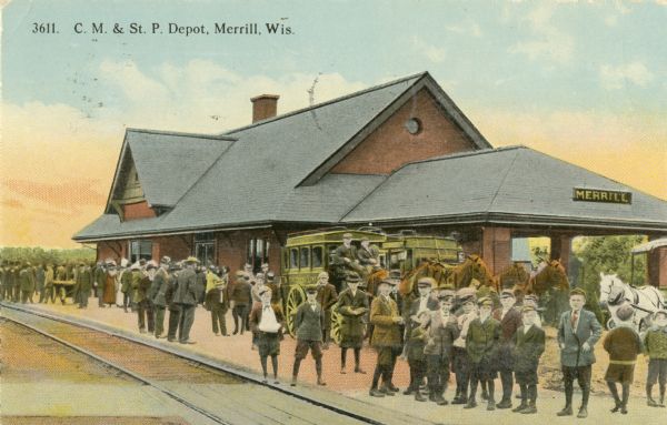 Colorized view of a crowd at the Chicago, Milwaukee & St. Paul station. Caption reads: "C. M. & St. P. Depot Depot, Merrill, Wis."