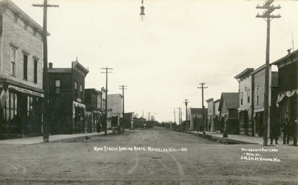 View down unpaved Main Street. Caption reads: "Main Street Looking North, Merrillan, Wisconsin".