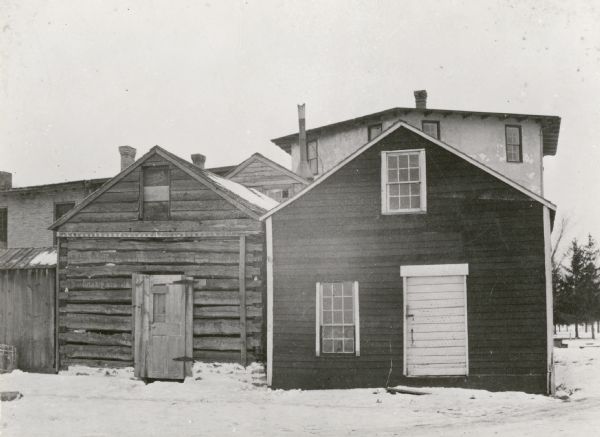 A view of a cabin and other buildings on the property of the Milton House, which was a part of the Underground Railroad prior to the abolition of slavery. The house was built in 1845 by Joseph Goodrich and turned into an Inn. The frame house and log cabin behind the Inn were also built by Goodrich, along with the Milton House Tavern. The Milton House was later taken over and turned into a museum.