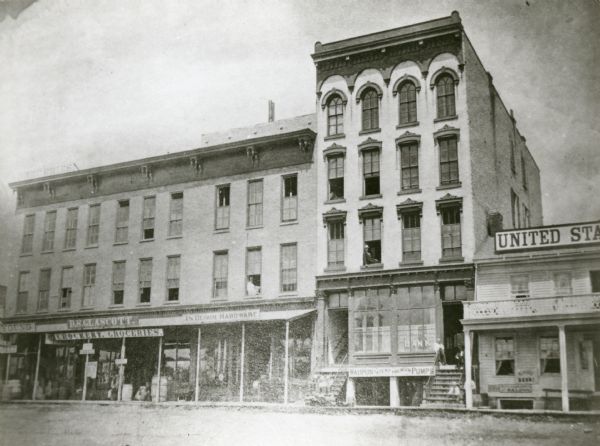 This photograph was made soon after the building was completed. It shows a five-leveled structure which was cut down to two and one-half levels in 1921. At right is the old United States Hotel built on site of the first Green County Courthouse, which burned down soon after its completion in 1840. At the left are three buildings, joined in a common front, which were built by Norman Churchill for a group of property investors. These structures remain adjoining the present First National building (1973). They will be removed when the bank expands to the west.