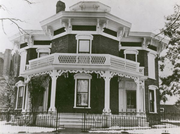 The Octagon House was built by General Francis Henry West. The photograph was taken late in 1930 and it shows the original "carpenter's lace" and other porch details before remodeling work was undertaken in 1969-1970. The materials were supplied by E.C. Hamilton for the Octagon House to be certified as a Wisconsin Landmark in 1971, and in "Bricks, Brackets, and Carpenter's Lace--19th Century Architecture in Monroe" by Hamilton in 1970. The present owner (as of 1973) is Rudolph F. Regoz.