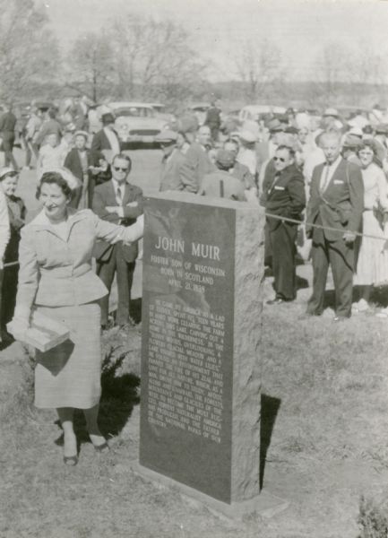 Historical marker at the site of John Muir's boyhood home, located in the John Muir Memorial Park near Montello. A woman stands next to the marker, and there is a crowd gathered in the background.