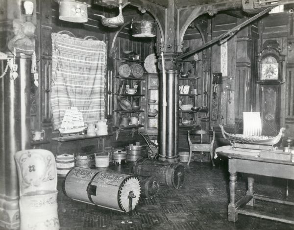 The interior of one of the buildings at "Little Norway," showing a group of objects of Norwegian decorative art and household utensils, including duck bowls, skis, mangletre, round boxes, kubbestol, bandestol, round trunks, and bowls.