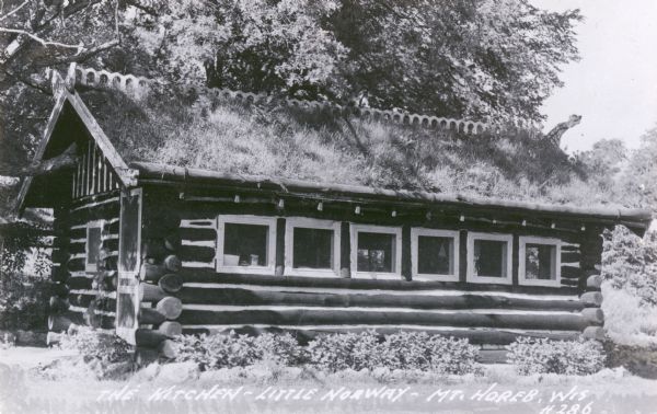 Exterior view of the kitchen at "Little Norway." Log building with a turf roof. Caption reads: "The Kitchen - Little Norway - Mt. Horeb, Wis."