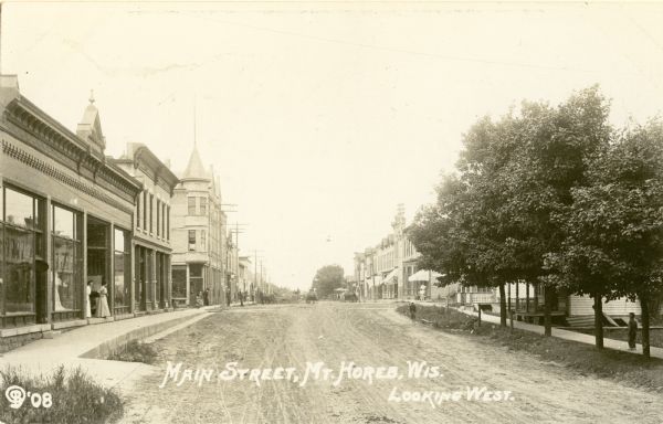 View down unpaved Main Street. Caption reads: "Main Street, Mt. Horeb, Wis. Looking West."