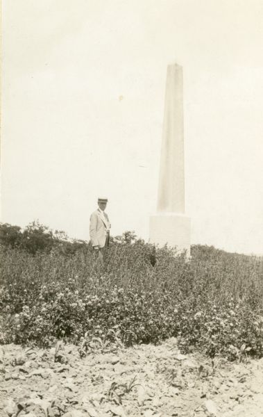 This 17.5 foot granite monument was erected in 1901 to mark the location of a Norwegian Lutheran Cemetery in Springdale Township. A man is standing near the monument.