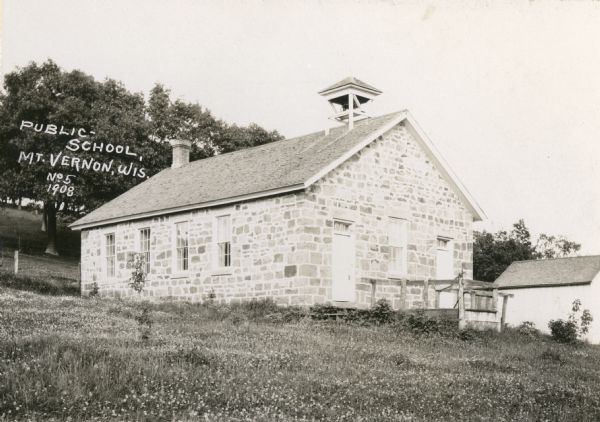 Exterior of public school made from stone. A bell tower is on the roof. Caption reads: "Public School, Mt. Vernon, Wis."