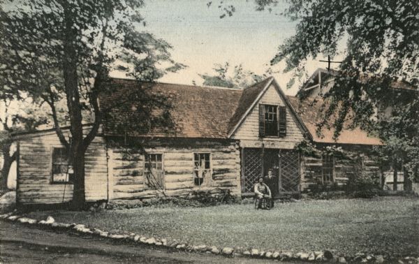 Governor Doty's log cabin. Two people are sitting and standing in the front yard.