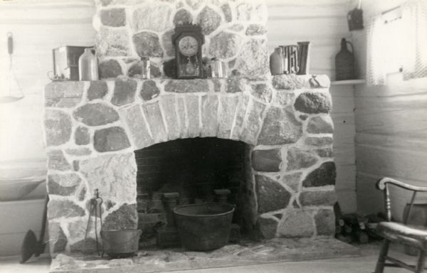 Fireplace in kitchen wing of the Doty Loggery, the home of James Duane Doty. A clock rests on the fireplace mantle, with a kettle on the hearth.