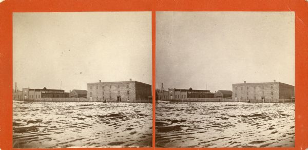 Stereograph view across what may be the Fox River, or a field with snow on the ground. There are large buildings behind a fence in the background. Caption reads: "Fox River view".
