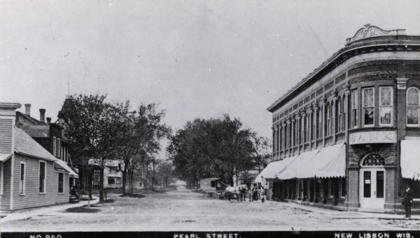 View of Pearl Street includes a horse-drawn carriage, a bank, other commercial buildings, and a man standing on the street corner. Caption reads: "Pearl Street, New Lisbon, Wis."