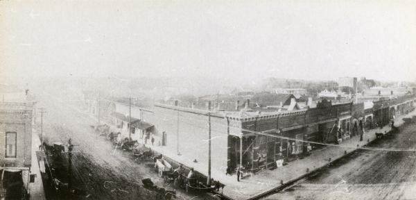 Elevated view of street, including horse-drawn carts and unidentified commercial buildings.