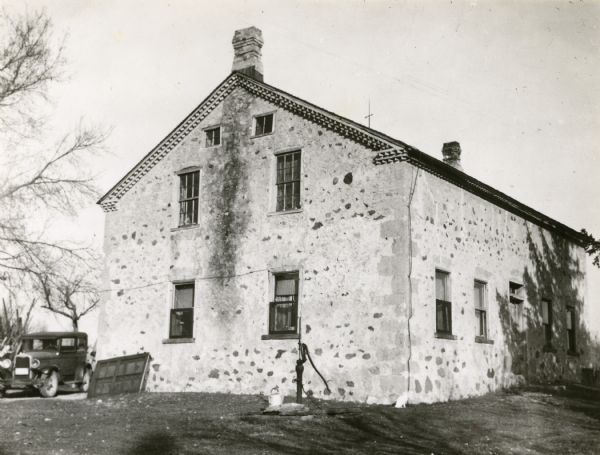 Weiss farm, residence of John Weiss, in the township of Saukville, Ozaukee County, one half mile from County Trunk Hwy Y near Washington County line. Side view of stone house with water pump and automobile in view.