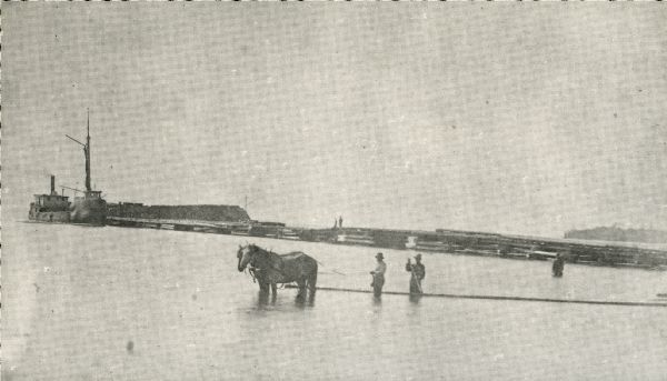 A view of a dock showing a steam vessel and men with a team of horses towing a log raft.