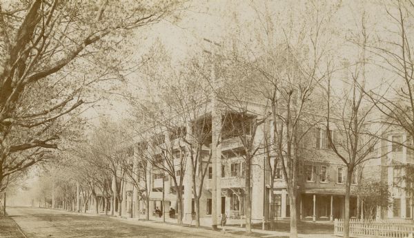 Side view of Draper Hall on Lake Road. Tree-lined street with two men sitting on chairs in front of Draper Hall.