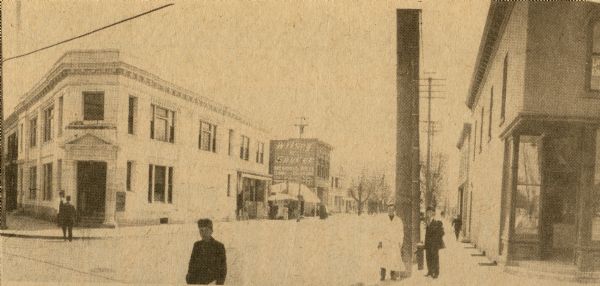 Clipping from <i>Oconomowoc Enterprise</i>. View of street corner includes shops and people. One sign reads: "Wilsey and Snyder."