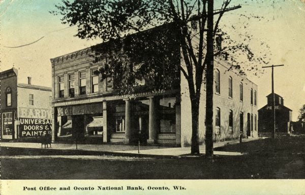View from street towards the Post Office and bank. An advertisement for a hardware store is on the side of the building on the left. Caption reads: "Post Office and Oconto National Bank, Oconto, Wis."