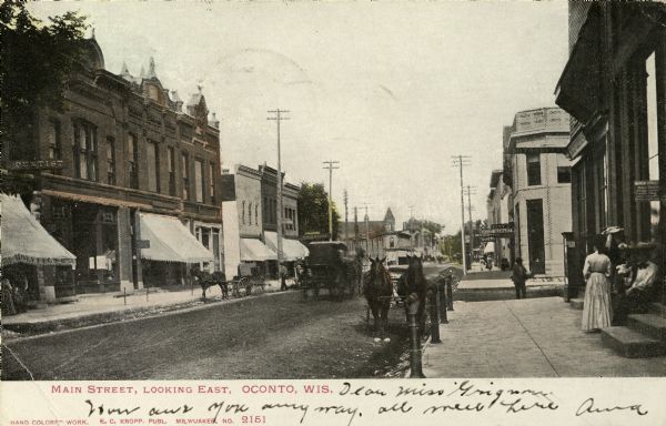 Main Street, looking east, people standing on sidewalk and horse-drawn carriages on street. Signs on one building read: "City Meat Market." Caption reads: "Main Street, Looking East, Oconto, Wis."