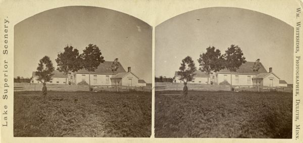 Stereograph of Presbyterian Mission school grounds in the Chippewa Indian reservation. Building in background, boy walking in field in foreground.