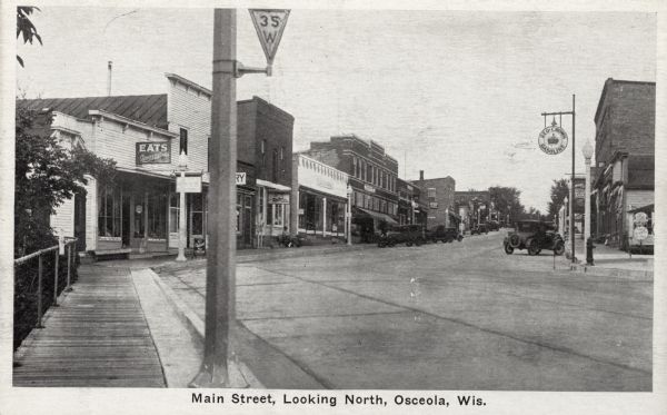 View from sidewalk on left side of bridge towards Main Street. Caption reads: "Main Street, Looking North, Osceola, Wis."