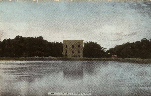 View across water towards the old mill building on the opposite shoreline. Caption reads: "The Old Mill, Osceola, Wis."