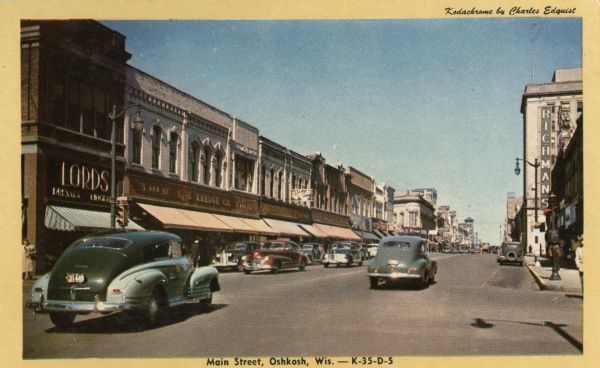 View of Main Street, with cars driving on both sides of the street. Commercial buildings are on the left. Caption reads: "Kodachrome by Charles Edquist: and "Main Street, Oshkosh, Wis."
