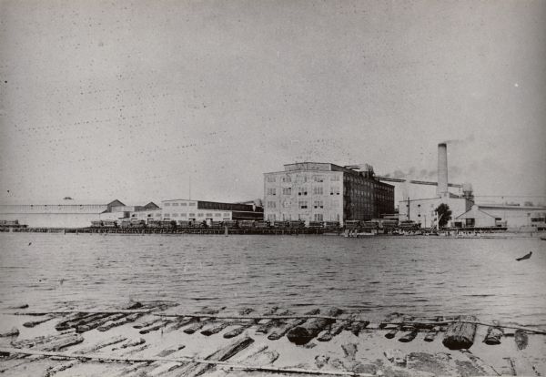 View of Paine Lumber Company from across the Fox River. Pilings are in the foreground. Founded in 1853 by Edward L. Paine, located on the east bank of the Fox River.