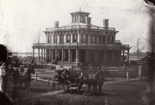View across street towards Senator Philetus Sawyer's residence. Sawyer was elected to the U.S. Senate in 1881. People are posing in horse-drawn vehicles in the foreground.