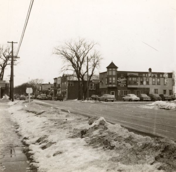 Snowy street. On the opposite side of the street is a sign on a building for "Repp's Bar".