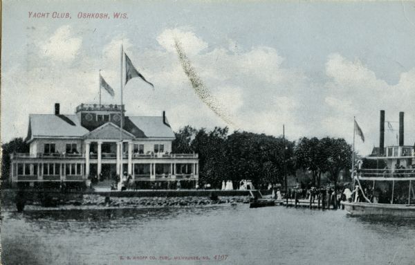 View across water towards the Yacht Club on the shoreline of Lake Winnebago. There is a widow's walk on the roof. A boat is near the pier on the right. Caption reads: "Yacht Club, Oshkosh, Wis."