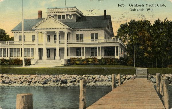 View down pier towards the Yacht Club on shoreline of Lake Winnebago. There is a widow's walk on the roof. Caption reads: "Oshkosh Yacht Club, Oshkosh, Wis."