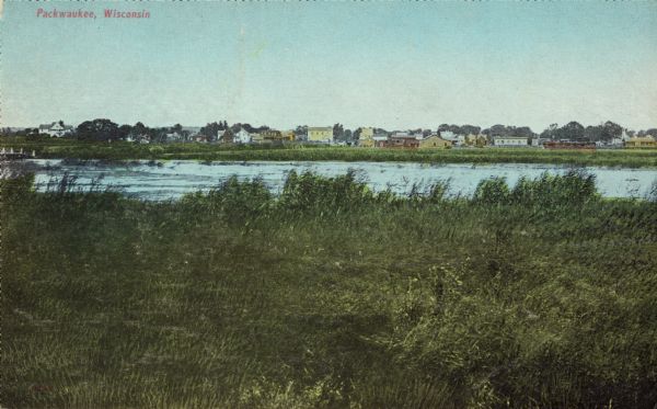 View of town behind a prairie field and a lake. Caption reads: "Packwaukee, Wis."