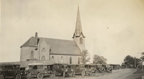 A view of a church, with automobiles lined up in front.
