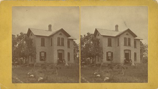 Stereograph of the Stewart home. The name I.N. Stewart is stamped on the back, and the home is presumably of the family of the donor of the photograph, Mary E. Stewart. A man and two women are posing on the front stoop. Another woman is standing on the left at the corner of the house.