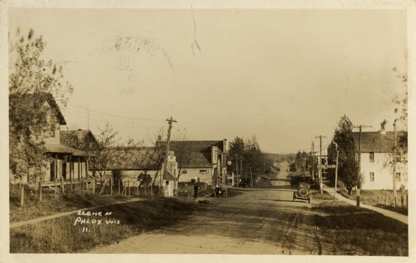 A view looking down an unpaved residential street. Caption reads: "Scene at Phlox Wis."