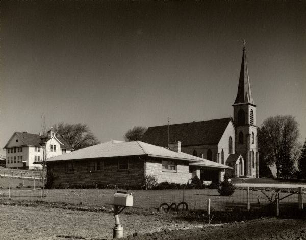 Exterior of residence, parochial school, and church. There is a mailbox in the foreground.