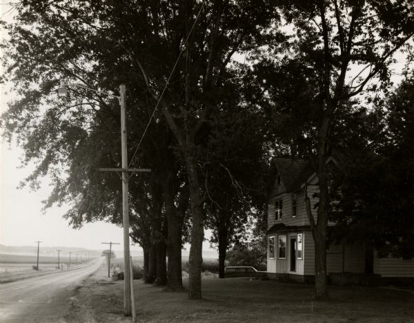 A view to the horizon looking down Mineral Point Road, with a country house on the right under trees, during early evening hours.