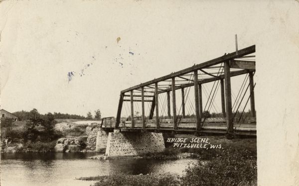 View from shoreline of a bridge across water. Caption reads: "Bridge Scene, Pittsville, Wis."