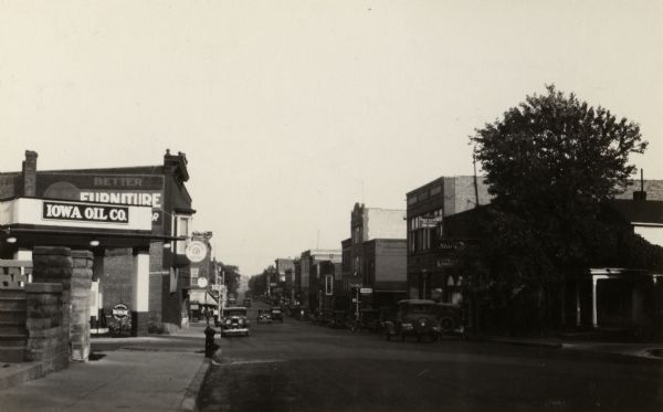 View looking down sidewalk on the left of Main Street. A sign in the foreground reads: "Iowa Oil Co."