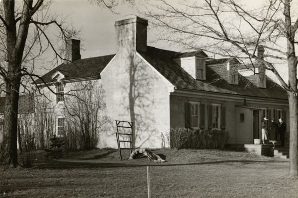 View across lawn towards the Mitchell-Rountree house. People are standing on the front steps of the house on the far right.