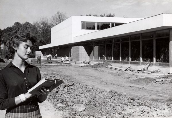 Wisconsin State College (later renamed the University of Wisconsin-Platteville). The Student Union is in final stages of construction, and in the foreground is Wisconsin State College student Jean Berryman who is looking down at a book in her hands.
