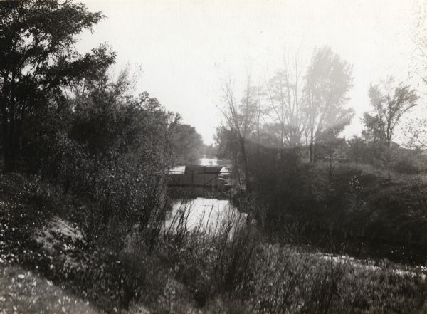 A view of the Portage Canal. In the immediate foreground is the Fox River, then the lower locks and the canal itself. The Indian Agency House may be seen through the trees to the right.