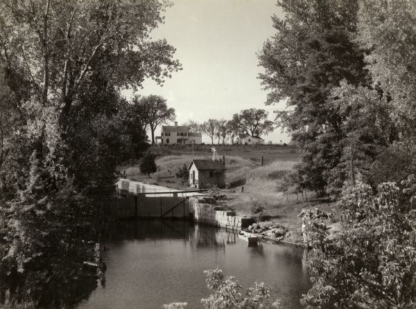 A view of the Portage Canal and lock. The Indian Agency House in the center background. The canal was dug in 1849 as part of the Fox-Wisconsin waterway project.