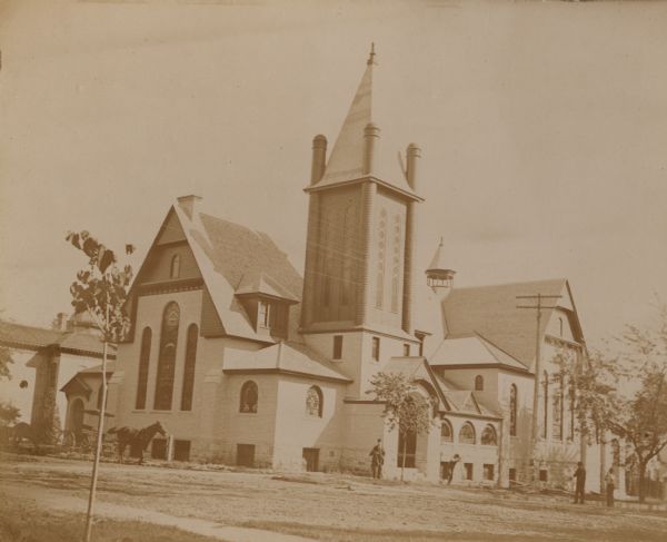 The First Presbyterian Church, dedicated October 15, 1893. There are horse-drawn carriages parked across the street on the left. People are standing near the church.