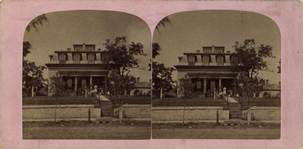 Stereograph of the Purdy house. View from street towards the house, with a stone wall along the sidewalk.