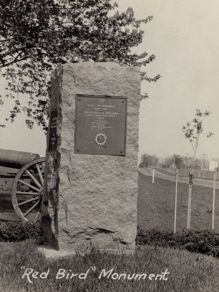 The Red Bird monument, erected on the site of Ft. Winnebago and Red Bird's surrender. There is a cannon on the lawn behind the monument. A road is along the right.