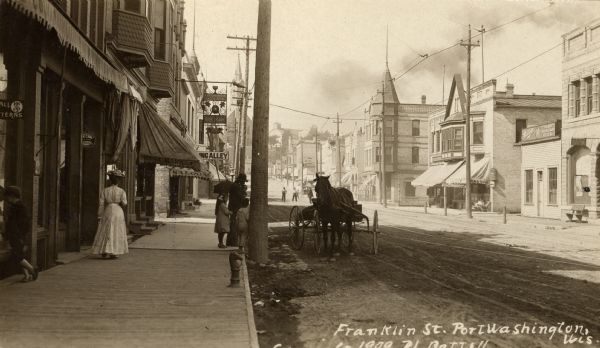 View down sidewalk along the left side of Franklin street. A horse-drawn vehicle is along the curb, and people are on the sidewalk. Caption reads: "Franklin St. Port Washington, Wis."