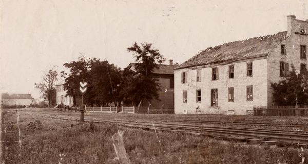 View across railroad tracks towards the offices of the American Fur Company. The roof is damaged or deteriorating.