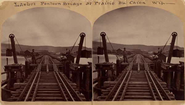 Stereograph of John Lawler's pile-pontoon railway bridge over the Mississippi River. Three men are standing and sitting on the bridge in the foreground. Buildings are across the river on the other side of the bridge. Caption reads: "Lawler's Pontoon Bridge at Prairie Du Chien Wis.__"